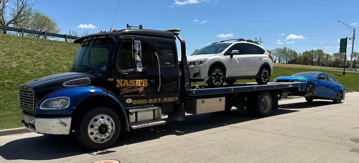 A tow truck carrying two cars on a sunny day.