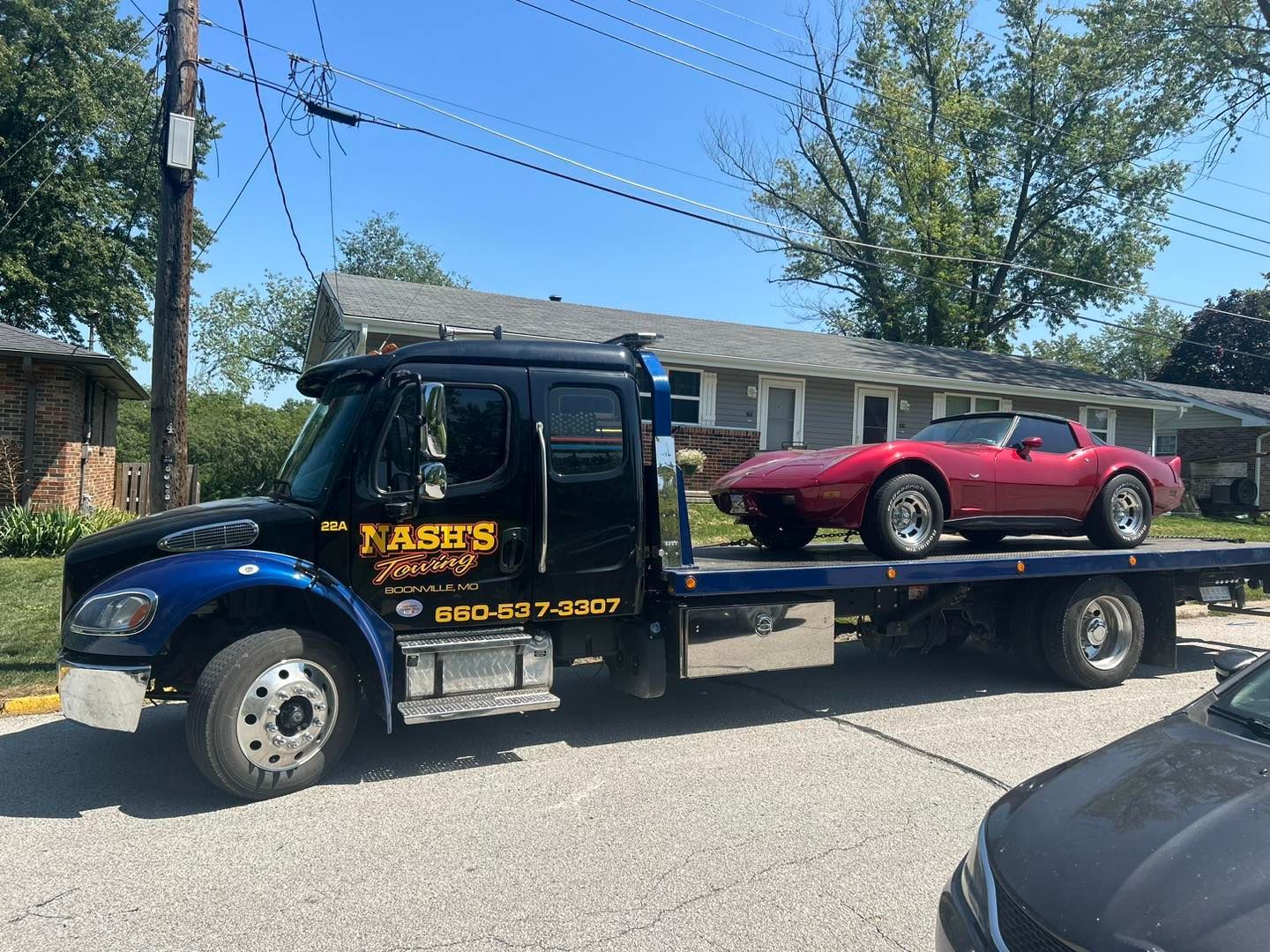 Tow truck hauling a red classic Corvette on a sunny street.