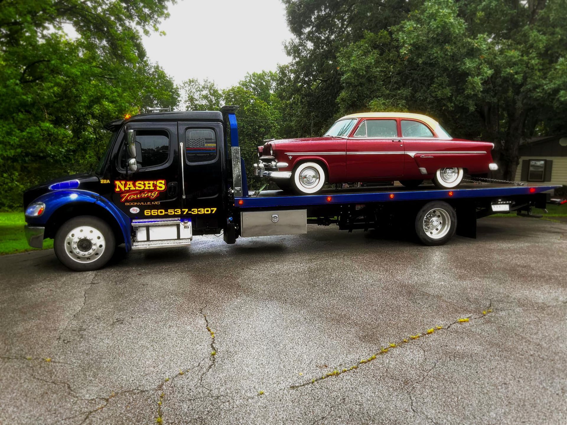 Red classic car being towed on a blue flatbed tow truck. Truck is black and blue with white lettering.