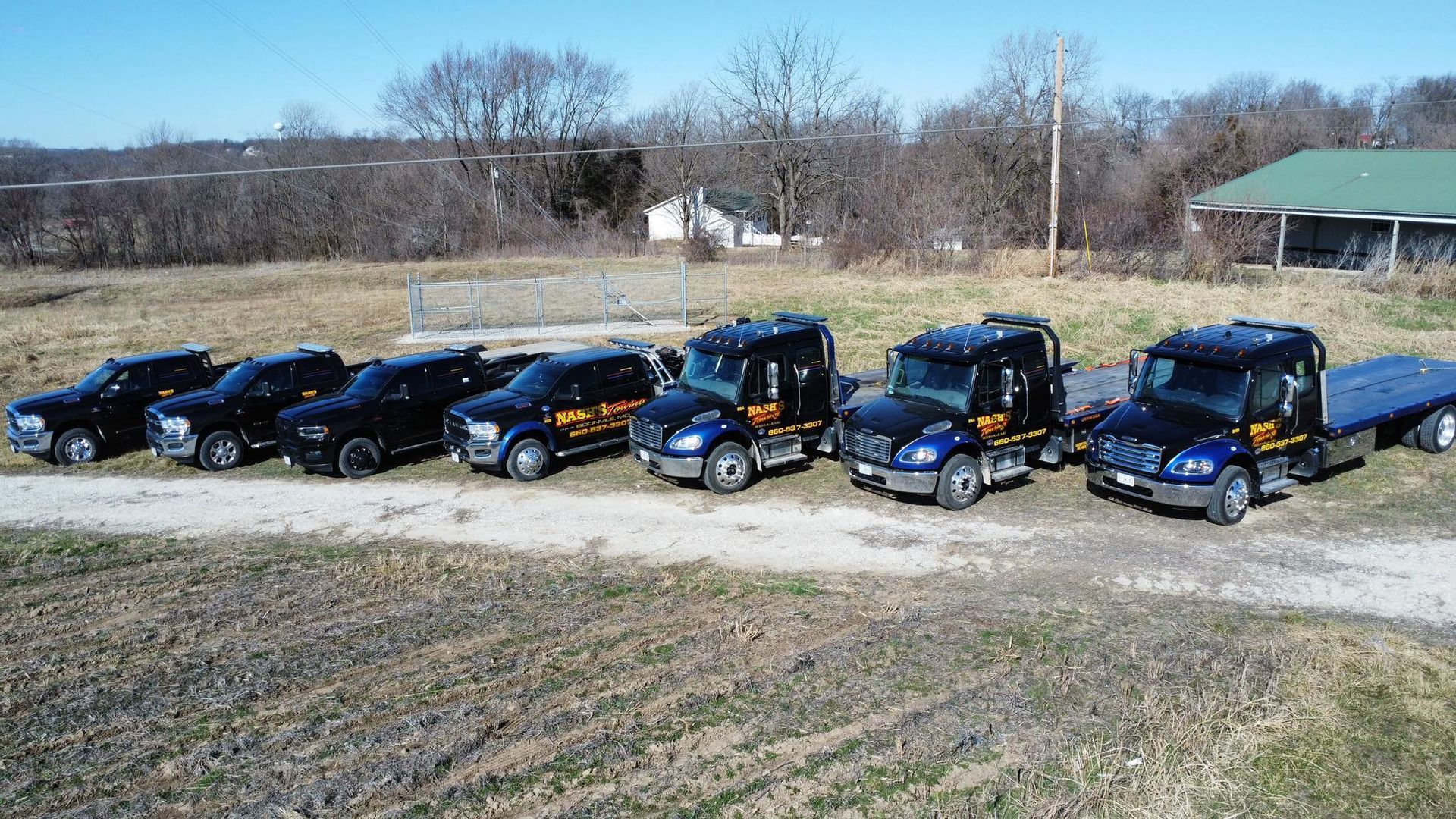 Lineup of tow trucks and pickup trucks on a grassy area, sunny day.