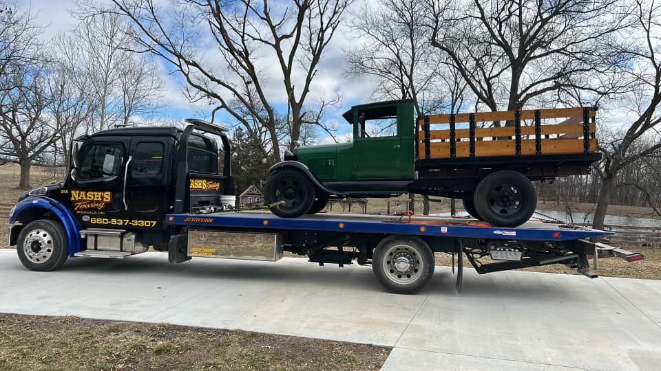 Tow truck carrying a green vintage pickup truck on a flatbed.