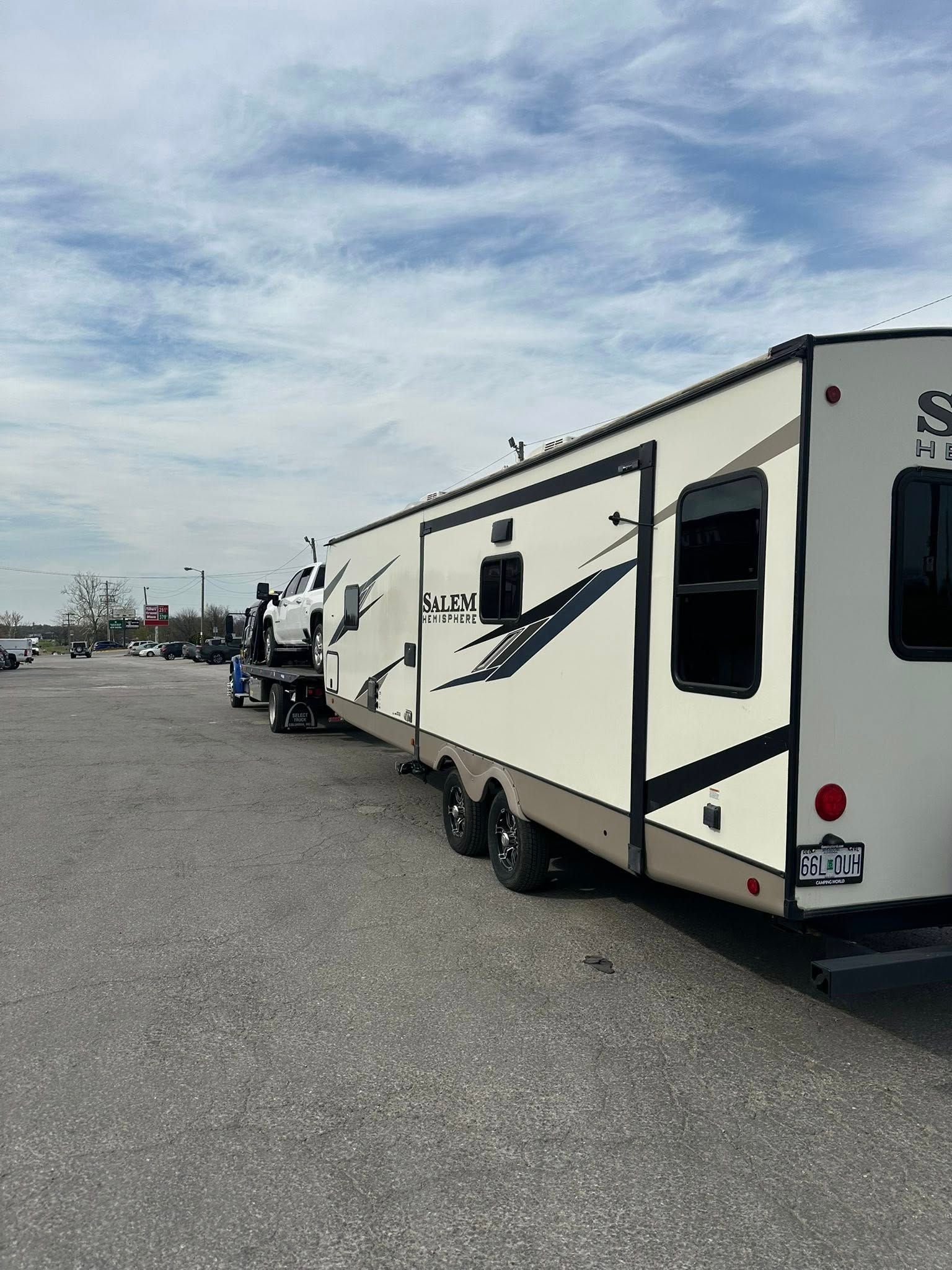 RV trailer being towed by a truck in a parking lot on a cloudy day.