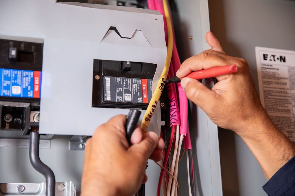 Person labeling electrical wires inside an electrical panel with a marker.