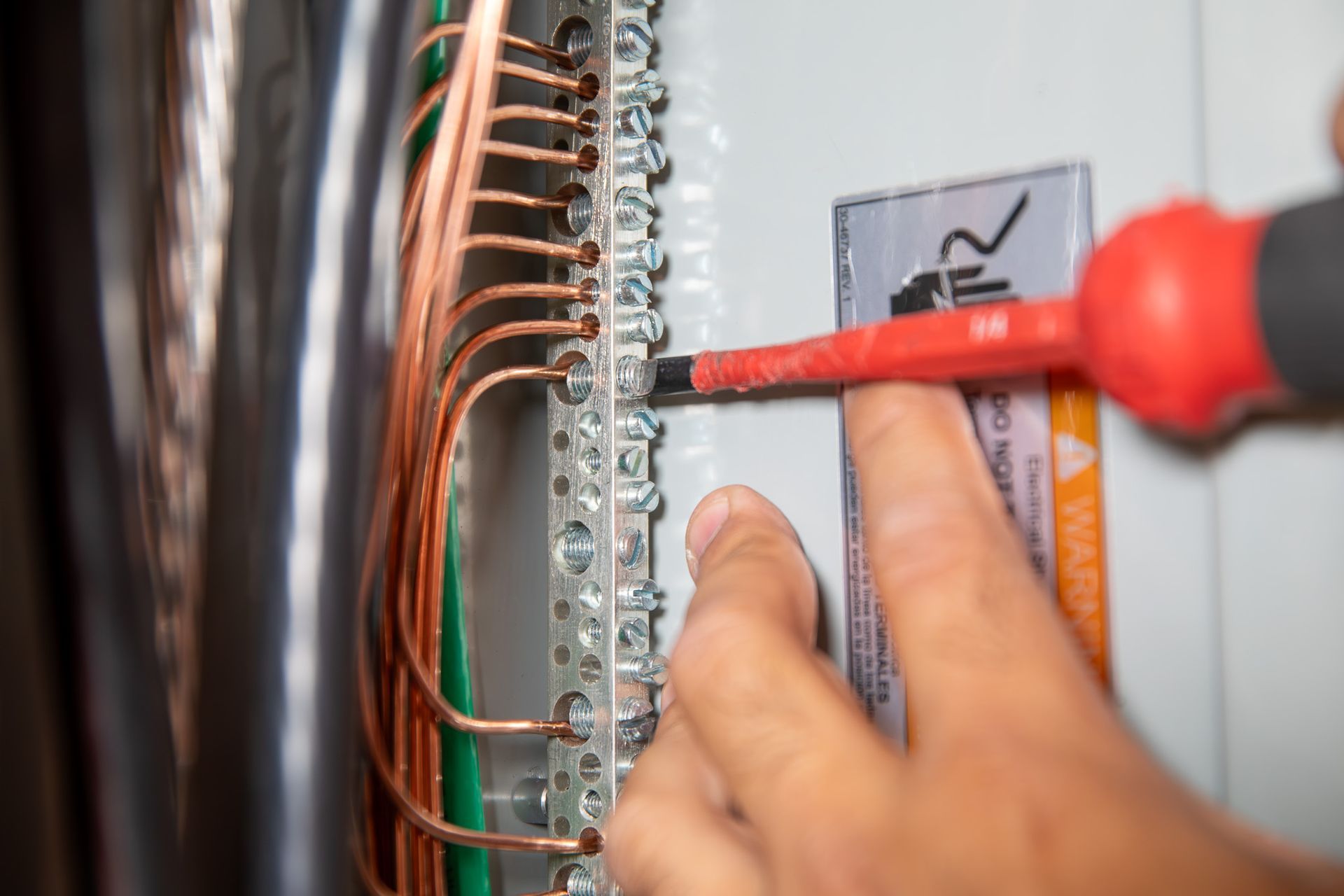 Person using a screwdriver to tighten wires in an electrical panel. Copper and green wires visible.