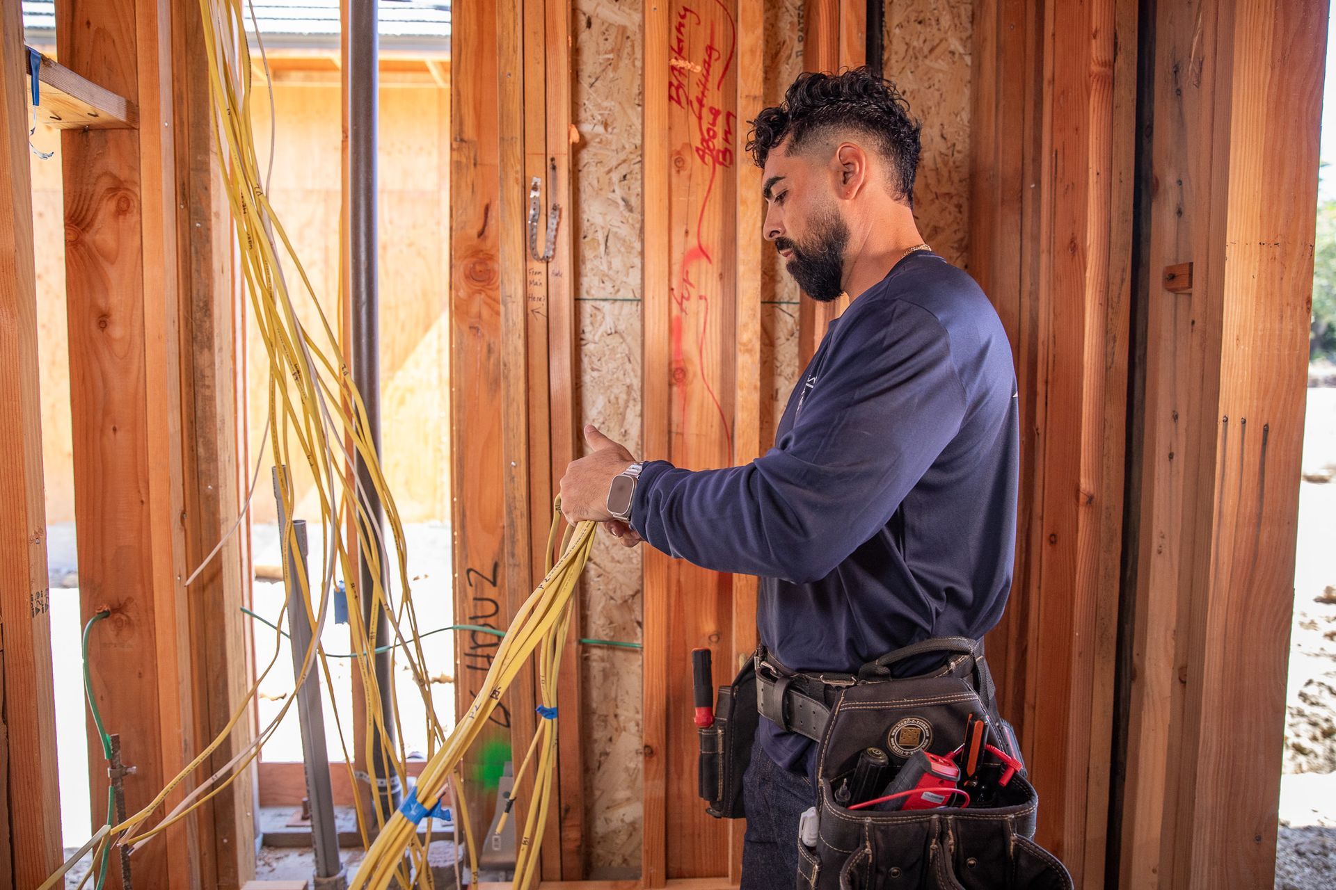 Electrician with yellow wires, standing in wooden frame of a house.