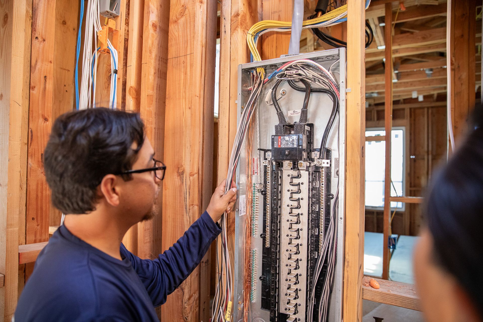 Electrician inspecting electrical panel in a wooden-framed wall during construction.