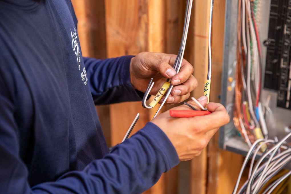 Electrician using wire strippers on electrical wires at a breaker box.