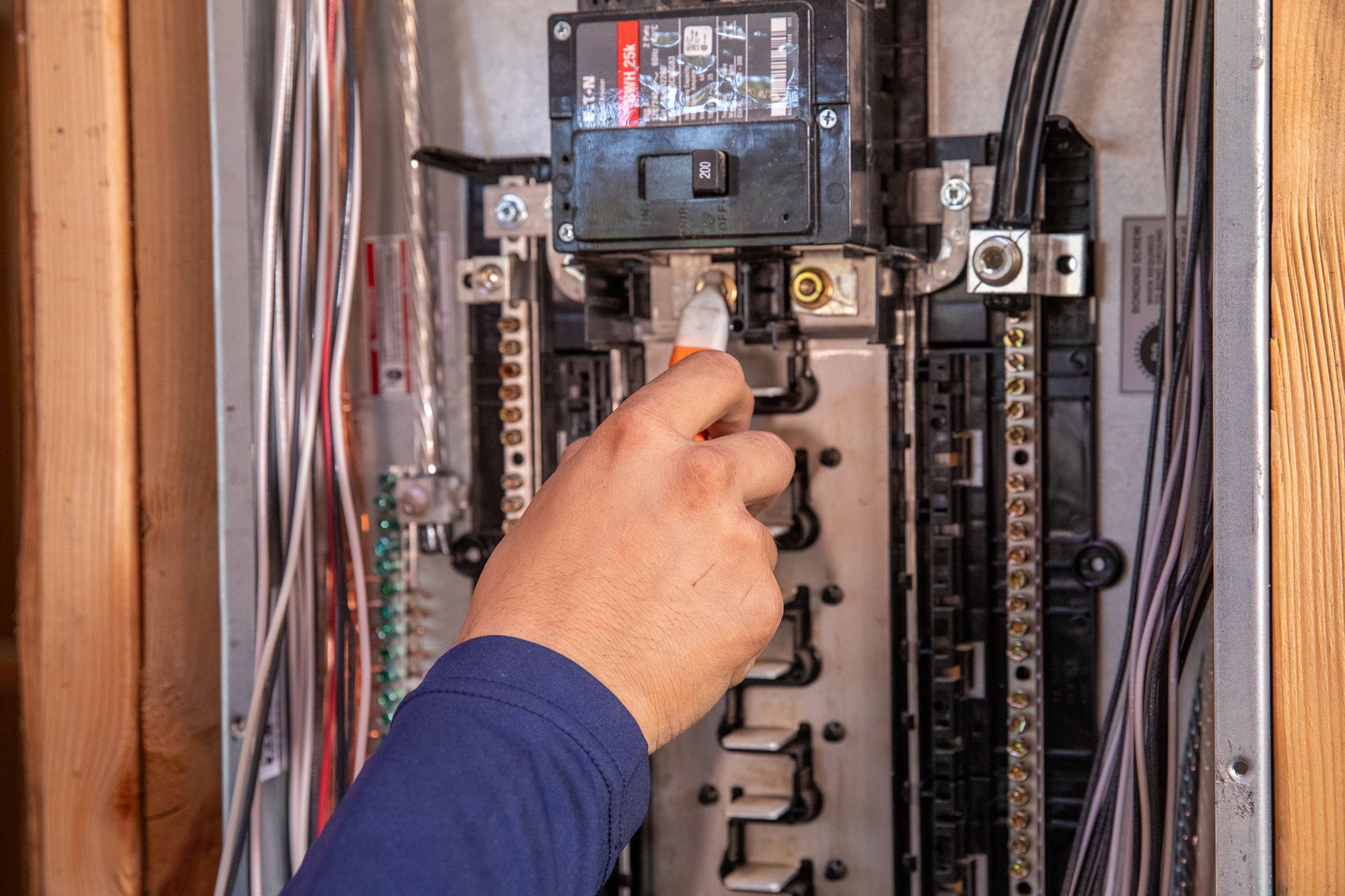 Hand testing a residential electrical panel with a voltage tester.