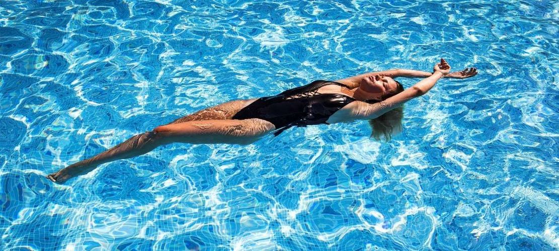 A Woman In A Black Swimsuit Is Floating On Her Back In A Swimming Pool — Pool Concepts in Howard Springs, NT