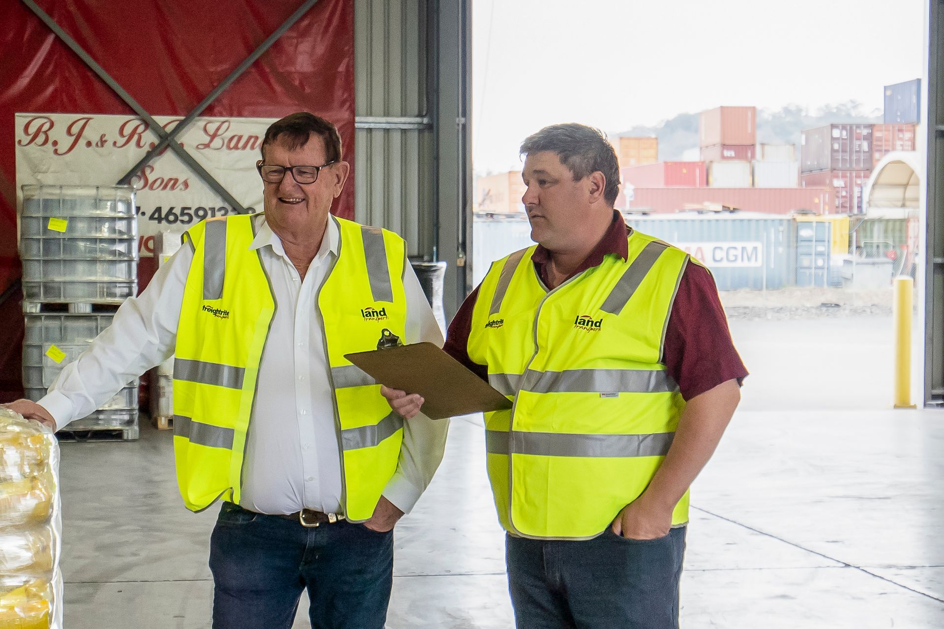 two men in yellow vests are standing next to each other in the land transport warehouse warehouse