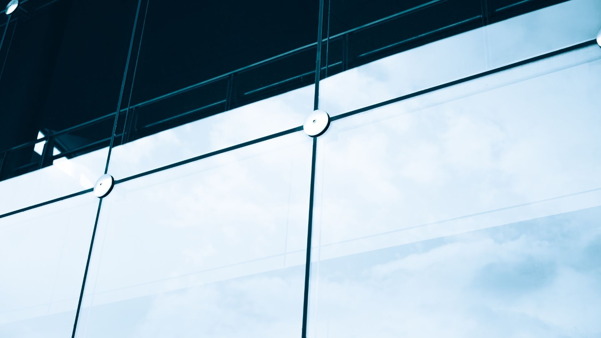 A grid-like glass curtain wall of a modern building with metal structural bolts against a blue sky.