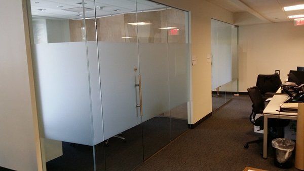 An office hallway featuring a glass-walled conference room with frosted privacy panels and a desk area on the right.