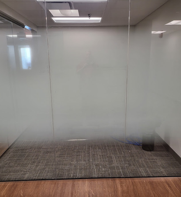 A modern office conference room with frosted glass walls, gray carpet, and overhead lights.