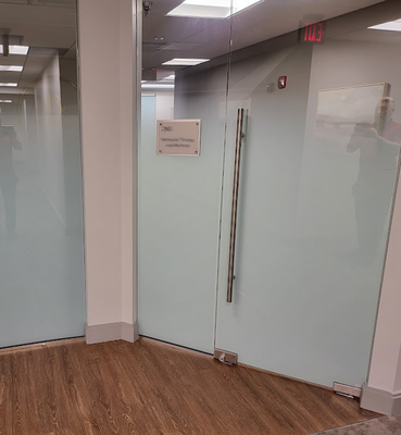 A glass office door with a silver handle, featuring a sign for “Speech Therapy and Audiology” on a wood-floored hallway.