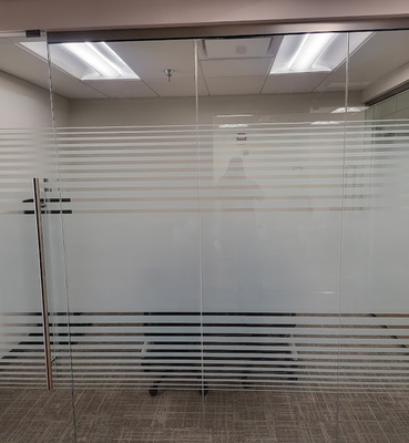 A glass office partition wall featuring a horizontal frosted-stripe privacy film pattern over a carpeted room.