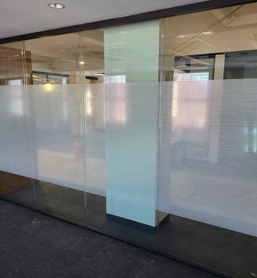 A glass office partition features a horizontal frosted band across the middle, with a solid light-colored central pillar.