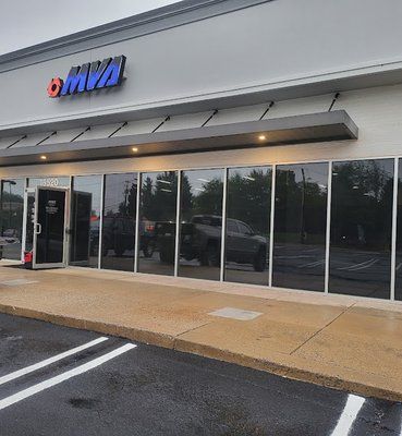 Exterior view of an MVA office with a gray facade, glass windows reflecting a parking lot, and a covered entryway.