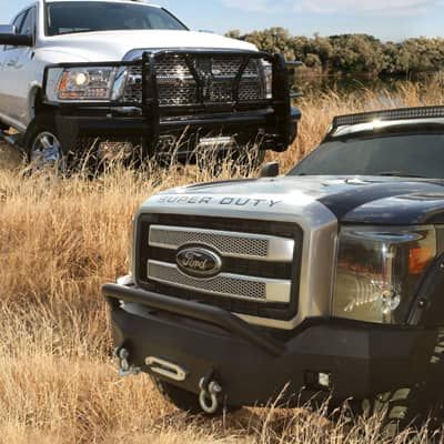 photo of two trucks in field with rugged front bumpers