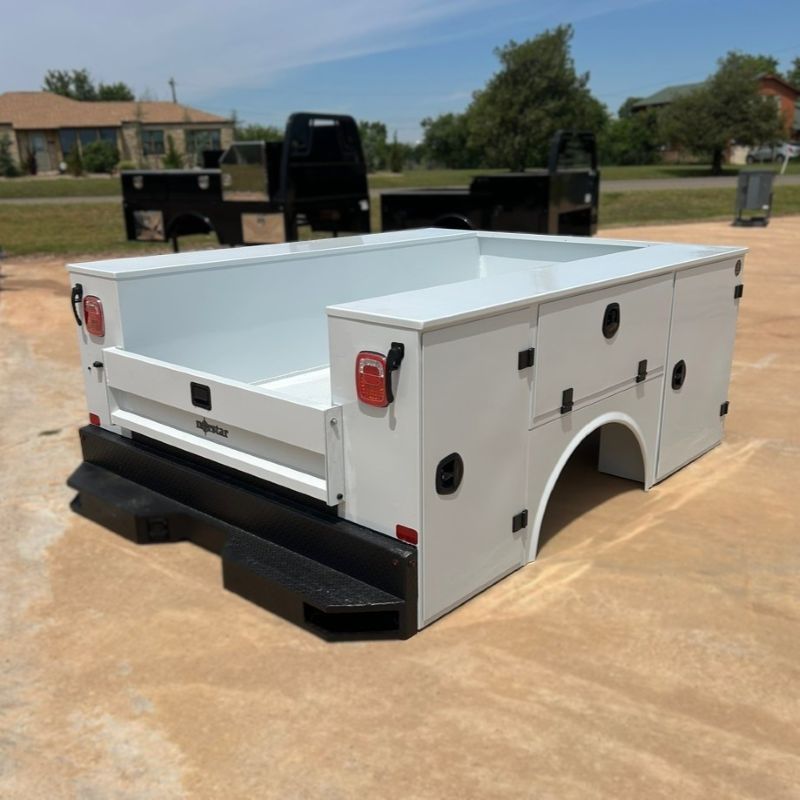 White utility truck bed with black bumper, parked outdoors on pavement.