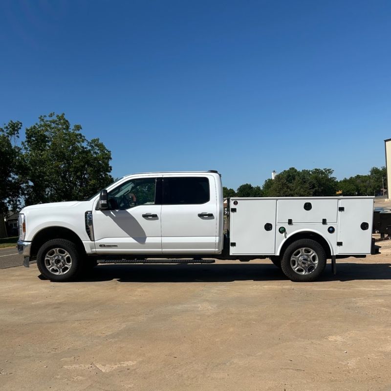 White utility pickup truck with tool compartments parked on a dirt lot under a clear blue sky