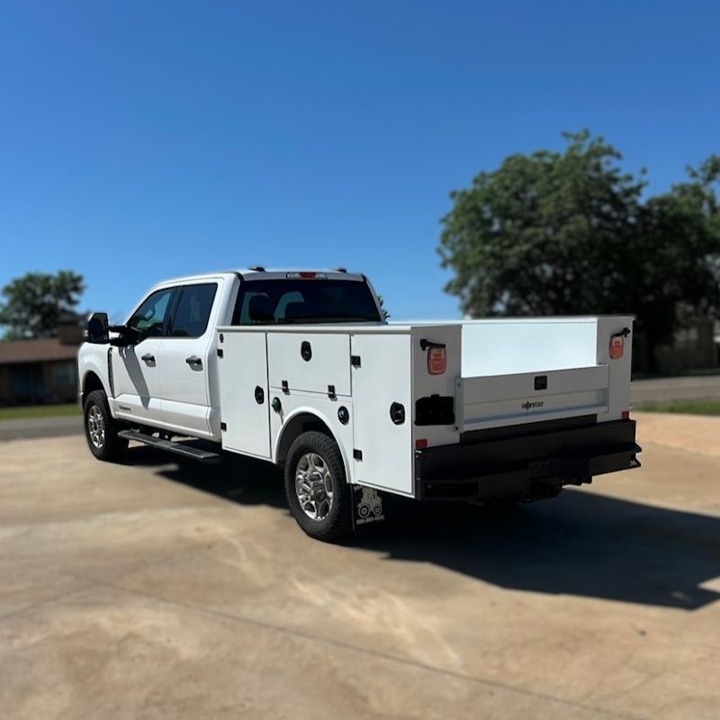 White service pickup truck with side compartments parked on a concrete lot under a clear blue sky.