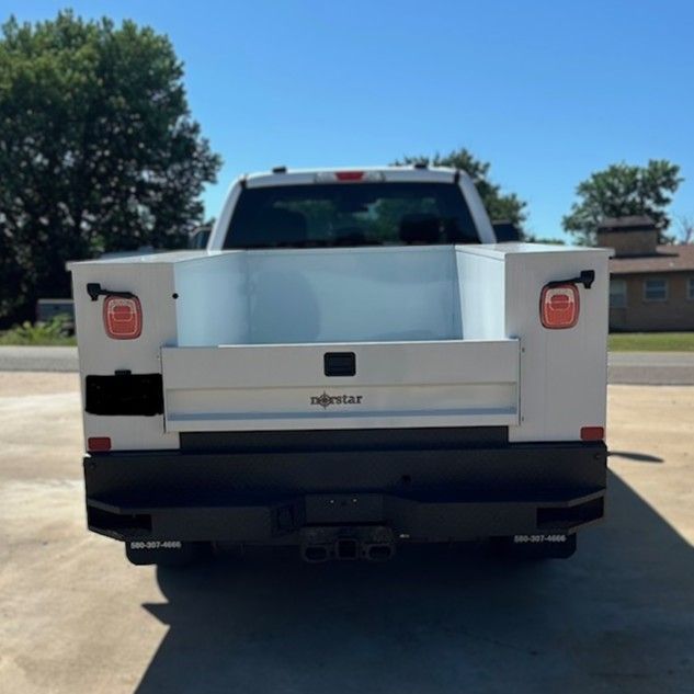 Rear view of a white utility truck parked on a sunny street, with black bumper and red taillights.