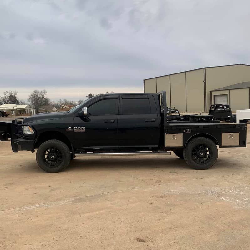 a black truck is parked in a dirt lot in front of a building .