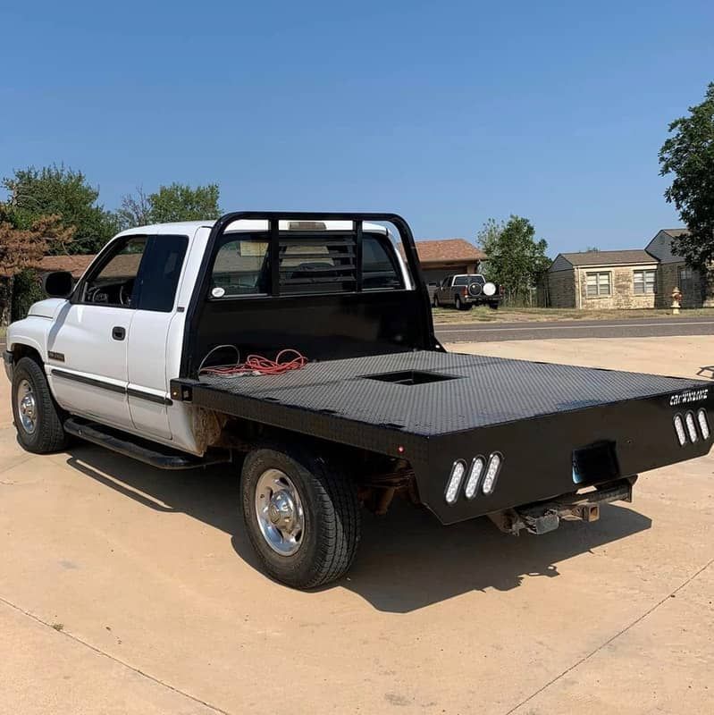 a white ram truck with a flat bed and gooseneck hitch is parked on the side of the road .