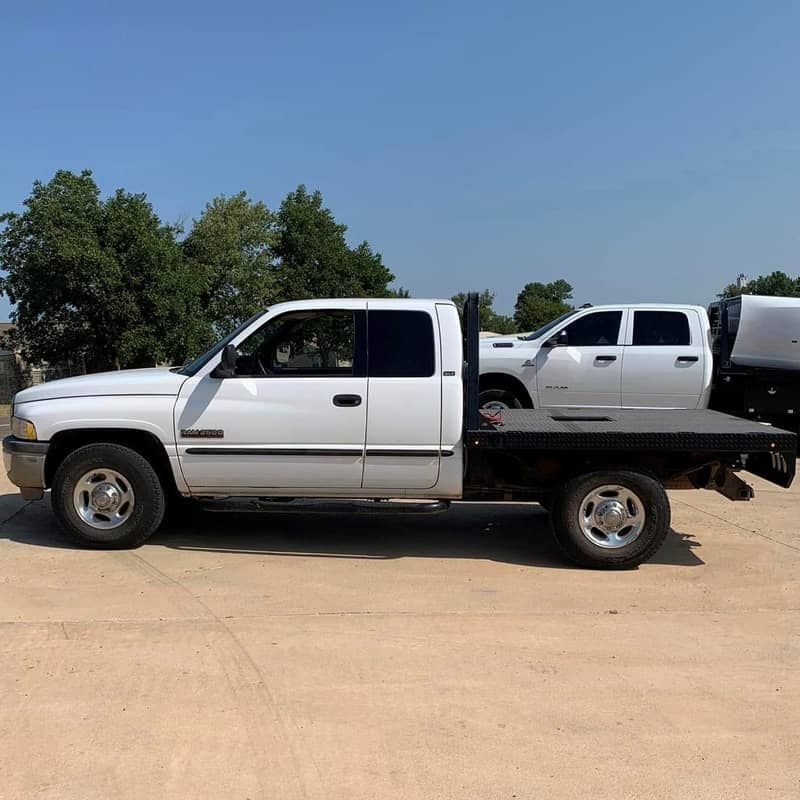 a white doge ram extended cab truck with a black flat bed is parked in a parking lot