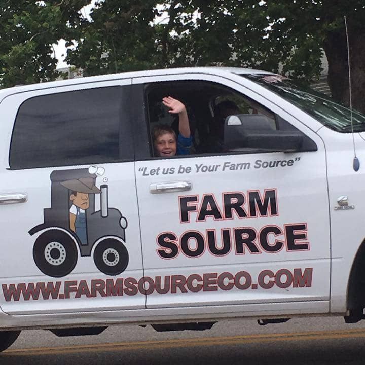 white truck with Farm Source text on truck door with child waving from truck window