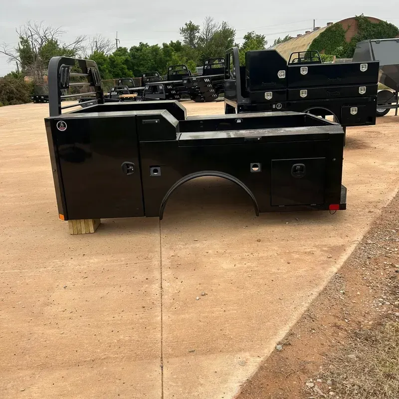 Black work bed with open top parked on a concrete lot, with stacked equipment trailers in the background