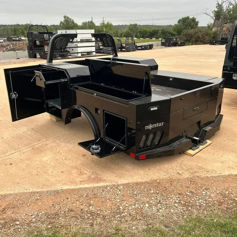 Black service body with open side door and raised bed, parked on a concrete lot outdoors.