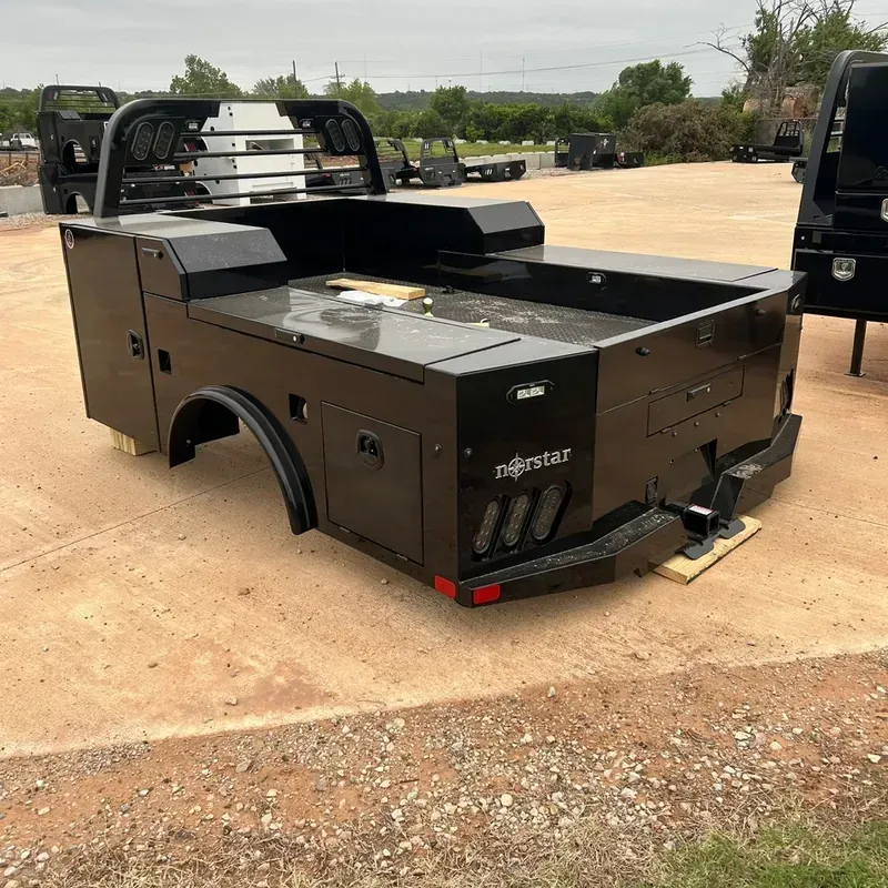 Black utility truck bed with storage compartments and ladder rack on a concrete lot