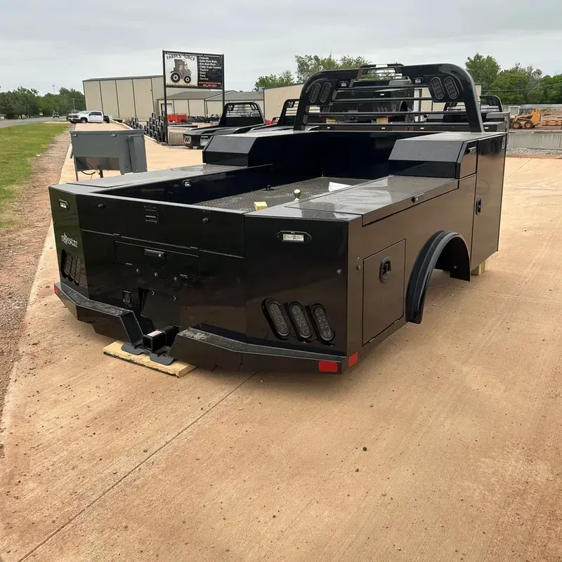 Black custom utility truck bed on a dirt lot, front-left view, with a flat front and mounted roll bar.