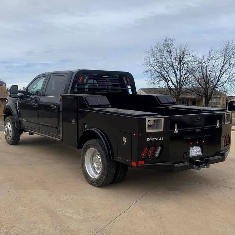 a black ford truck with a skirted flat bed with tool boxes is parked in a parking lot .