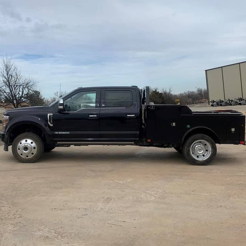 a black ford truck with a flatbed bed with toolboxes is parked in a dirt lot .