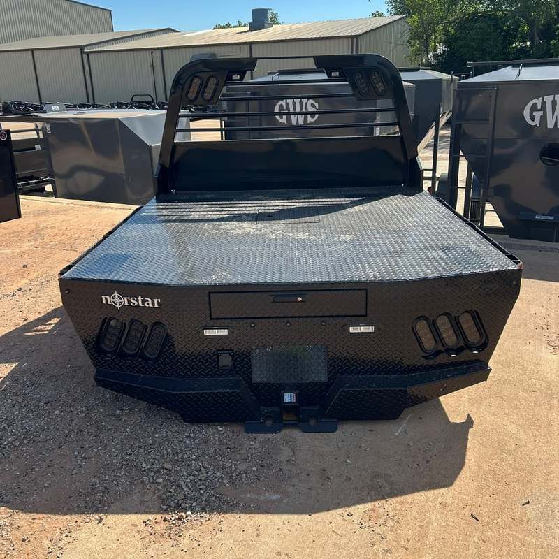 Black truck bed flatbed parked outdoors on gravel lot.