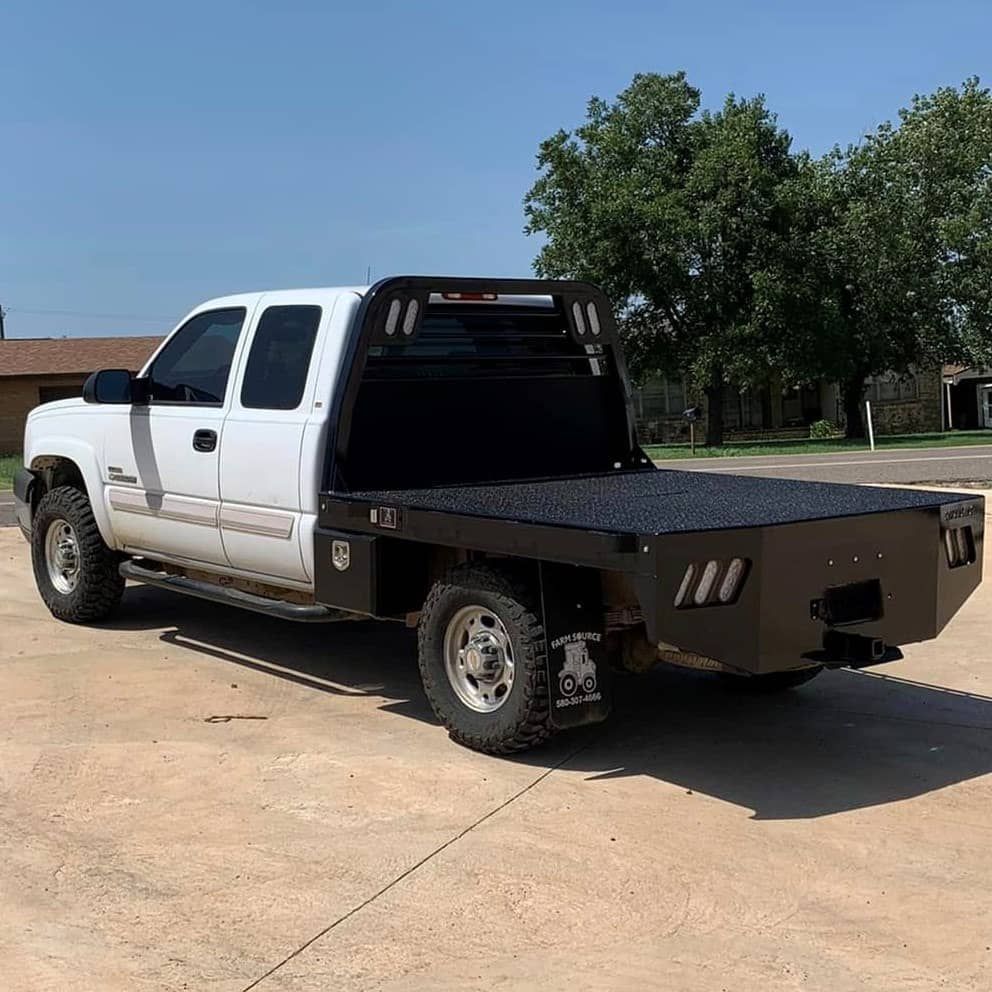 a white chevrolet truck with a flat bed is parked on the side of the road .