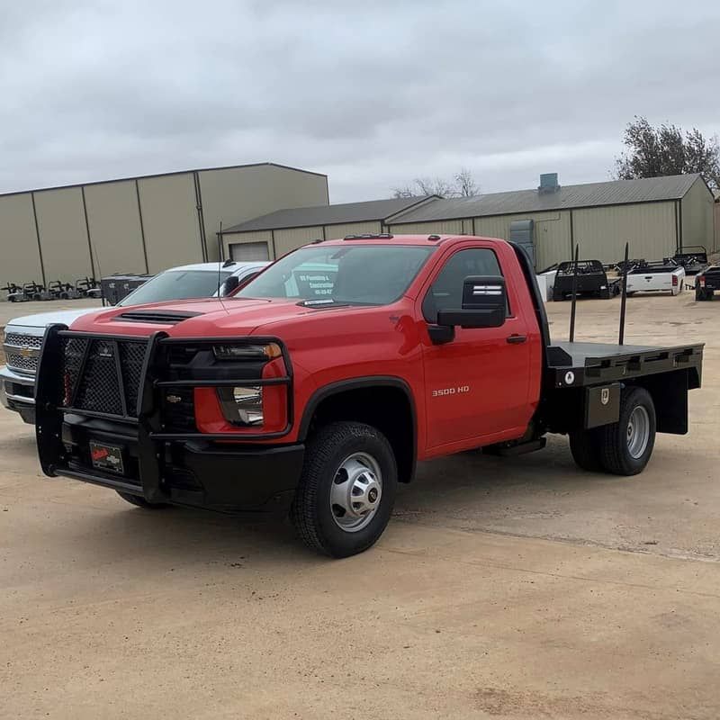 a red gmc truck with a crownline bale flat bed is parked in a parking lot .
