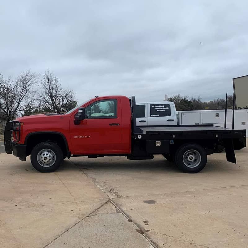 a red truck with a flat bed is parked in a parking lot .