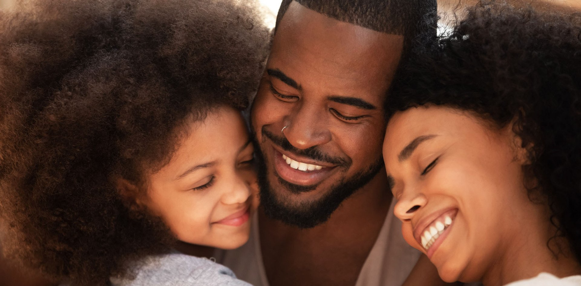 A man , woman and child are hugging each other and smiling.