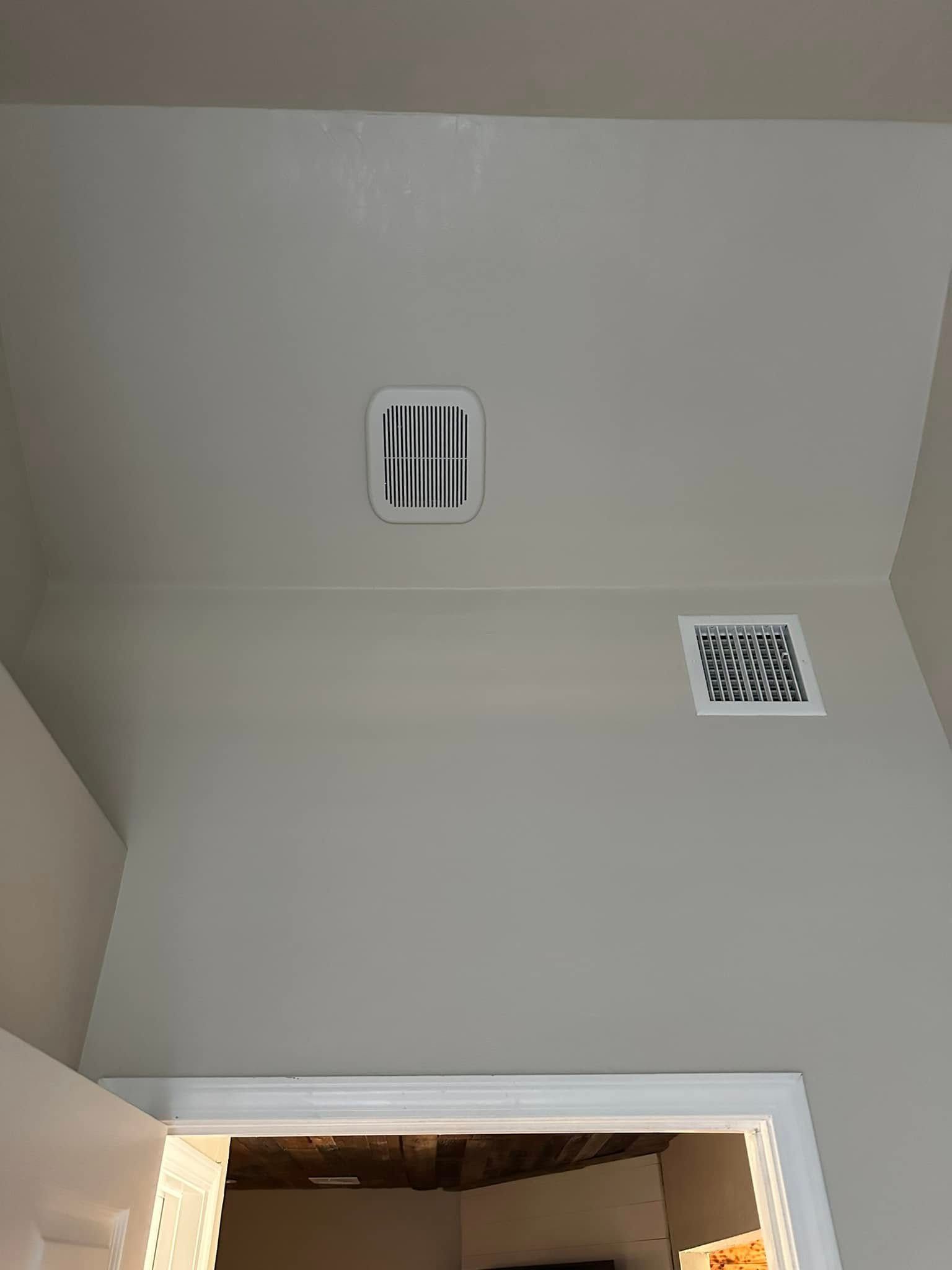 A room with a door and a vent on the ceiling.