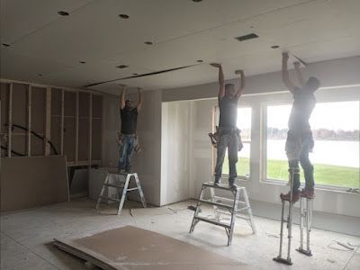 Three men are working on a ceiling in a room.