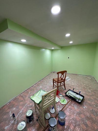 A room with green walls and a chair and buckets of paint on the floor.