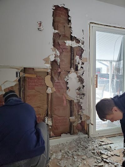 Two men are working on a wall in a room.