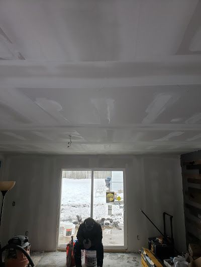 A man is working on the ceiling of a living room.