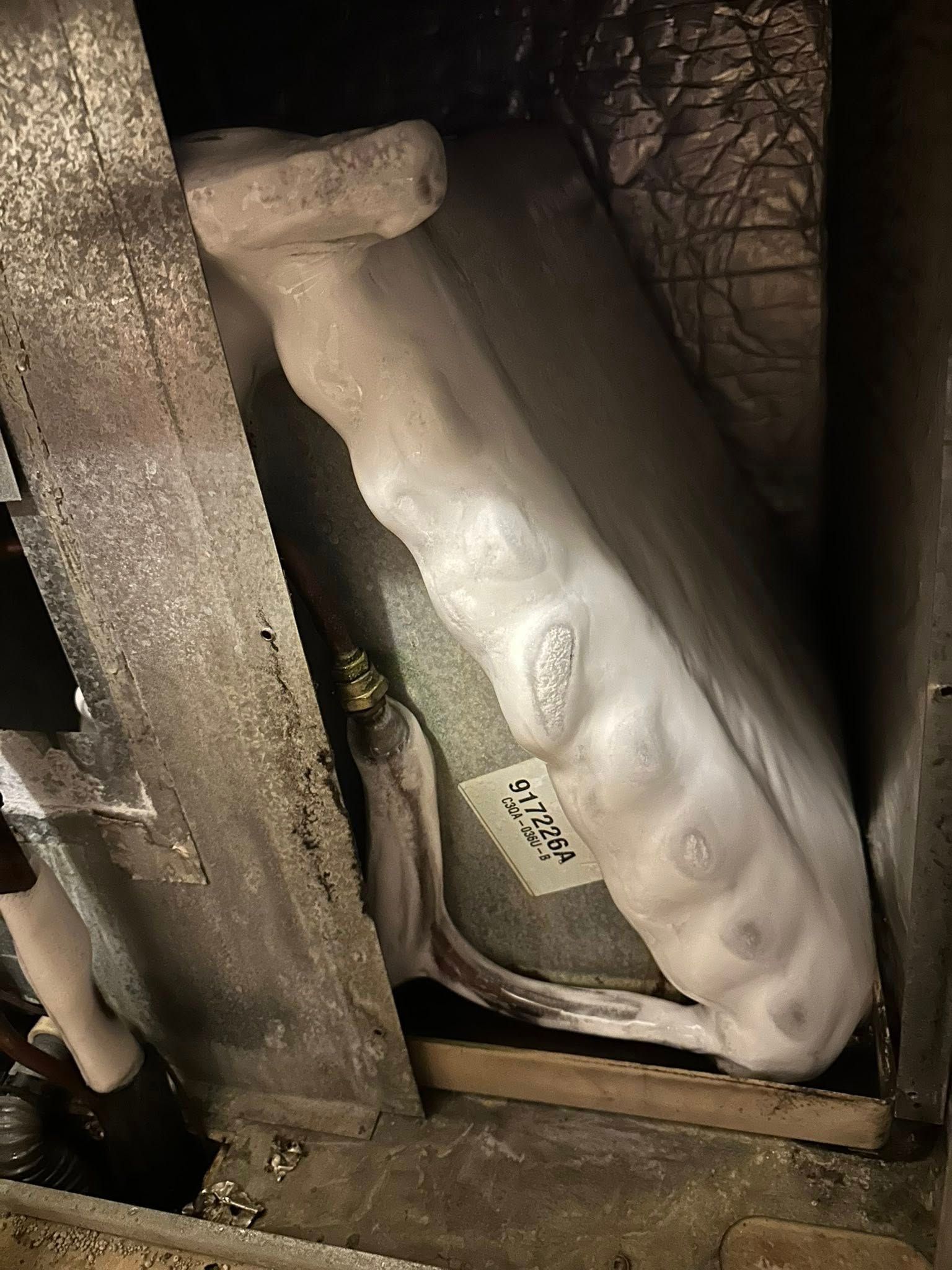 A frozen HVAC evaporator coil inside a metal furnace housing.