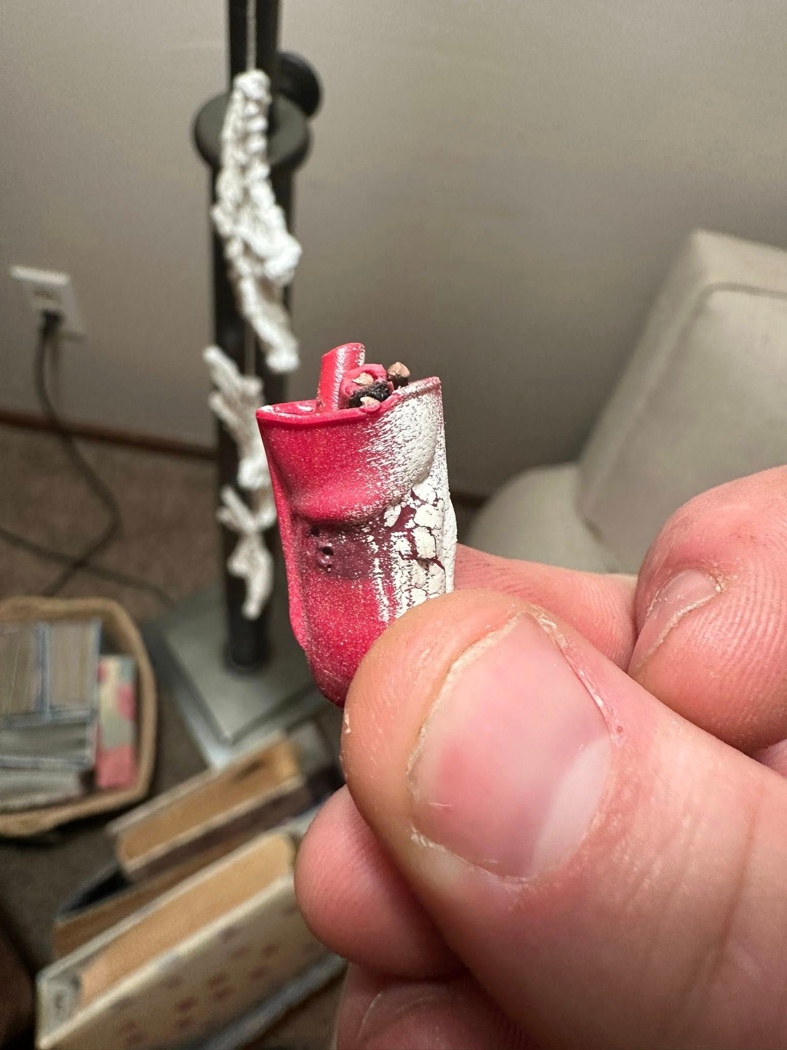 A close-up of a person holding a broken, red and white plastic piece from a broken object over a blurry room background.