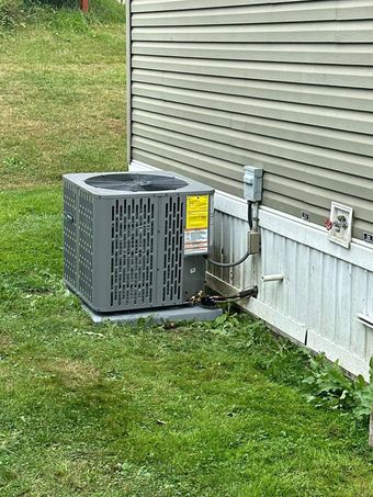 A grey outdoor air conditioning unit sits on a concrete pad next to the tan siding of a house.