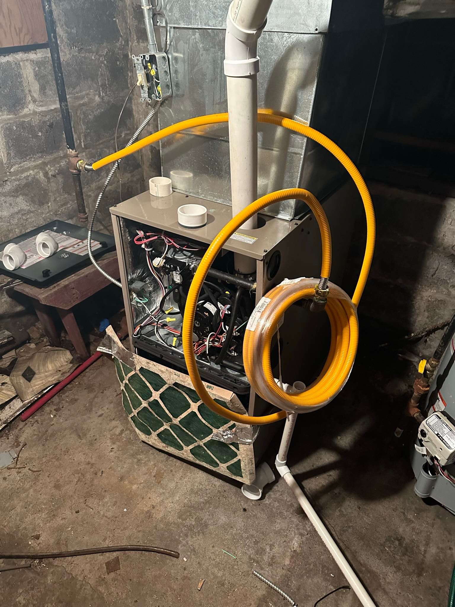 A natural gas furnace in a basement with a yellow flexible gas line coiled and connected to the unit.
